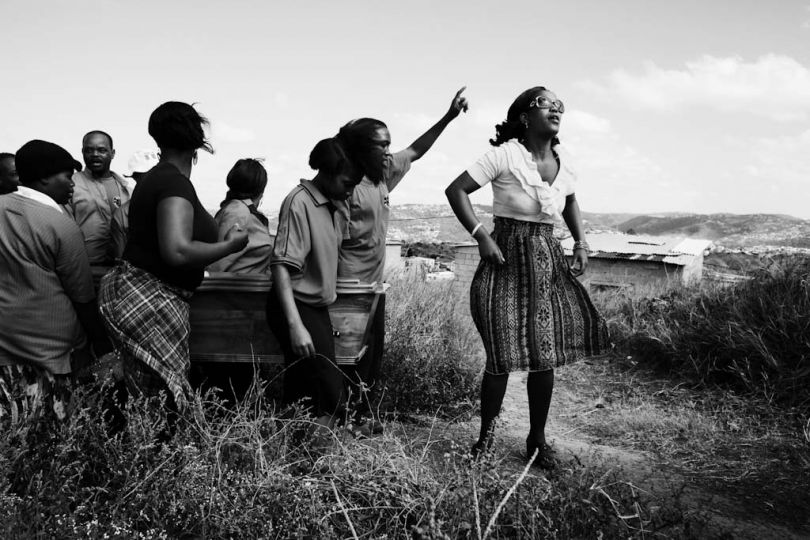 Brightness Sishi, 25 (right), leads the funeral procession for her aunt Thembi Veze, along with her brother, Bongumenzi Knowledge Sishi, 15. Thabsile and Bongumenzi have been living with their aunt and her three children in the Richmond Farm Transit Camp near Durban since 2009. u201cIn the camp, I can't say it's nice to stay here- there's no park, nowhere to play soccer, nowhere to rest,u201d says Bongumenzi. u201cIt's too dangerous. There's no security. We are waiting for moving - they are still building the RDPs. They said we would be here two years.u201d © Krisanne Johnson