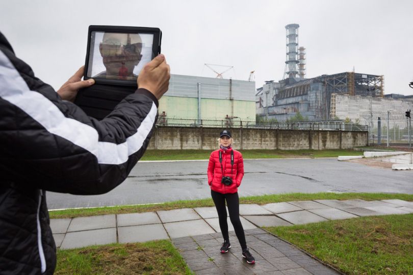 [CNPP, Chernobyl Exclusion Zone, Ukraine, 2013] During a one-day visit to the Exclusion Zone, tourists only have a few minutes to snap photographs of themselves in front of the sarcophagus that encases the failed reactor # 4. Its western wall, leaky and unsound because it was hastily erected after the accident, has recently been stabilized. u201cThis is as close as you can get, hurry up,u201d announces the tour guide. Radiation is still so high that he asks visitors to stay on the paved paths u201cas radiation is substantially higher on the grass.u201d / [CNPP, Chernobyl Exclusion Zone, Ukraine, 2011] Durant une visite d'un jour à la zone d'exclusion, les touristes n'ont que quelques minutes pour faire des photos d'euxmêmes devant le sarcophage qui protège la nature du réacteur # 4. La paroi ouest, fi ssurée et instable, car rapidement installée après l'accident, a été stabilisée récemment. --Ne vous approchez pas davantage, dépêchez-vous--, annonce le guide. Le rayonnement est encore si élevé qu'il demande aux visiteurs de rester sur les chemins cimentés --car le rayonnement est sensiblement plus élevé sur le sol en herbe.-- © Gerd Ludwig / National Geographic Creative / National Geographic Magazinen