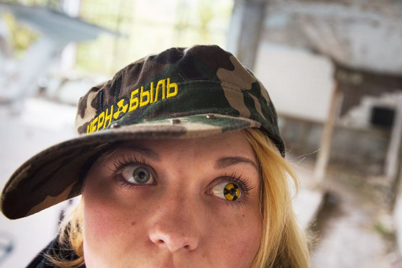 [Kopachi, Ukraine, 2013] Tourist guides have many ways to enhance the experience of visiting the Exclusion Zone and make it memorable. Vasilina Bas, 22, generally attaches a cosmetic contact lens depicting a radiation sign to one of her eyes, while wearing a Chernobyl cap, which is on sale in several shops in Chernobyl. [Kopachi, Ukraine, 2013] Pour rendre inoubliable la visite dans la zone d'exclusion, tous les moyens sont bons pour les guides. Vasilina Bas, 22, aime bien les lentilles cosmétiques, qui métamorphosent ses yeux brillants en symbole de rayonnement. Assortie à la lentille, elle porte une casquette Tchernobyl que l'on peut acheter dans quelques boutiques. © Gerd Ludwig / National Geographic Creative / National Geographic Magazinen