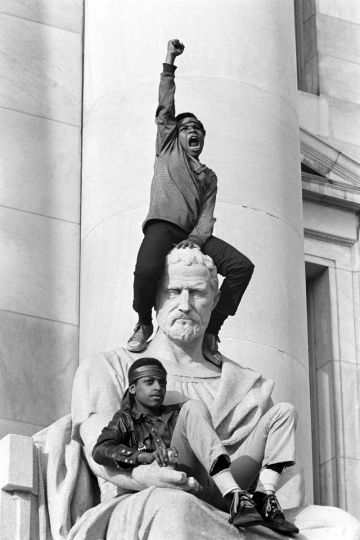 May 1, 1970 - New Haven, Connecticut, USA: Boy gives raised fist salute as he and a friend sit on a statue in front of the New Haven County Courthouse during a demonstration of 15,000 people during the Bobby Seale / Ericka Huggins trial. Bobby Seale, Chairman of the Black Panther Party is on trial along with Ericka Huggins for murder. Both are acquitted. (Stephen Shames/courtesy Stephen Kasher Gallery)