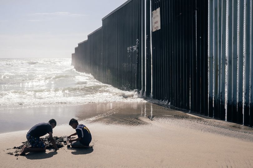 Deux enfants jouent dans le sable, à côté d'eux le mur qui sépare le Mexique des États-Unis. Le mur de Tijuana a été construit en 1994 et rend le passage de la frontière beaucoup plus dangereux pour les migrants. 08/05/2017 Tijuana, Baja California, Mexique. - Southern Border © Jeoffrey Guillemard