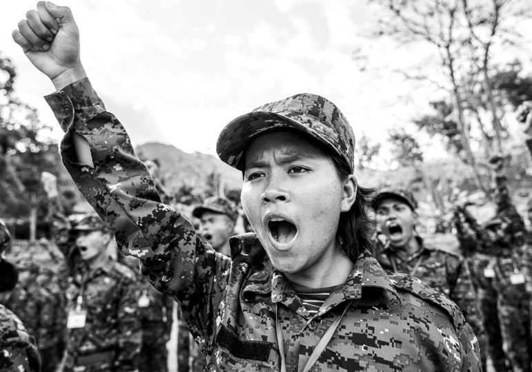 MYANMAR, Camp Victoria, État Chin, 28/11/2022. Une jeune fille crie au milieu des autres volontaires venus de tout le Chinland pour s’entraîner dans le camp Victoria, un camp militaire caché dans les forêts de l’ouest birman et géré par le Chin National Army (CNA), l’un des principaux groupes armés Chin qui lutte contre l’armée birmane. Ils étaient autrefois étudiants, enseignants, agriculteurs ou encore ingénieurs, et la plupart avaient participé aux manifestations massives qui avaient ébranlé le pays pour dénoncer la prise de pouvoir de la junte. Aujourd’hui, la lutte armée est leur unique option pour mettre en place un système démocratique et, surtout, protéger leur famille de la Tatmadaw, dont les exactions sont particulièrement impunies dans cette région à majorité Chrétienne, expliquent-ils. Ils n’ont parfois pas plus de 15 ans. Photographie de Robin Tutenges / Hans Lucas.
