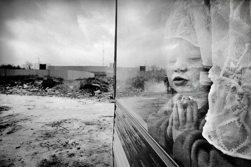 The border with the Republic of Ireland at Strabane. Traveller child in a caravan with the British Army border checkpoint behind. Northern Ireland 1990. © Mark Abrahams - Courtesy of Bluecoat Press